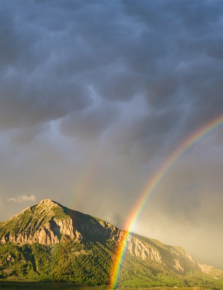 A vibrant rainbow passing in front of a lush green Colorado Mountain.